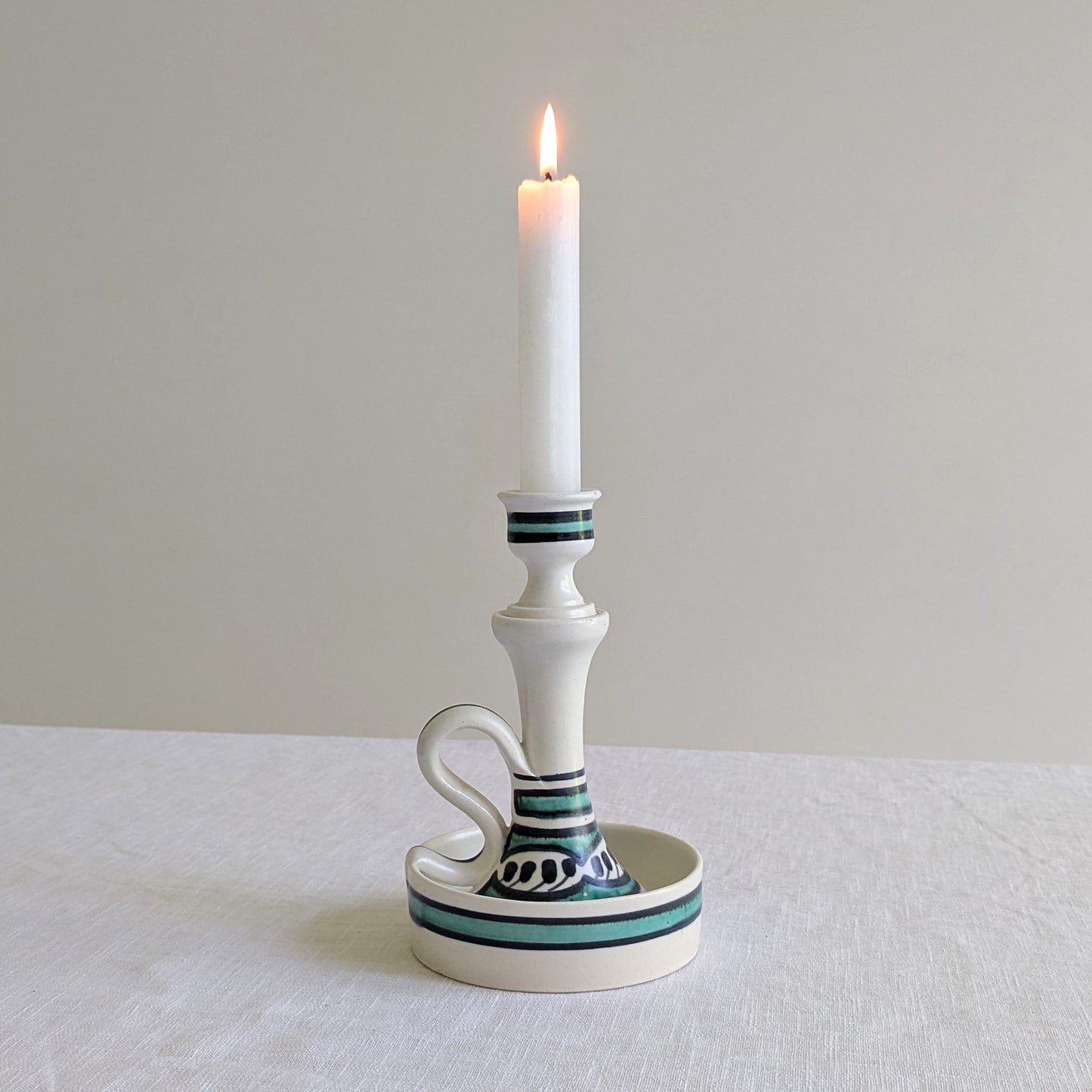 Tall white ceramic candle holder with a lit candle