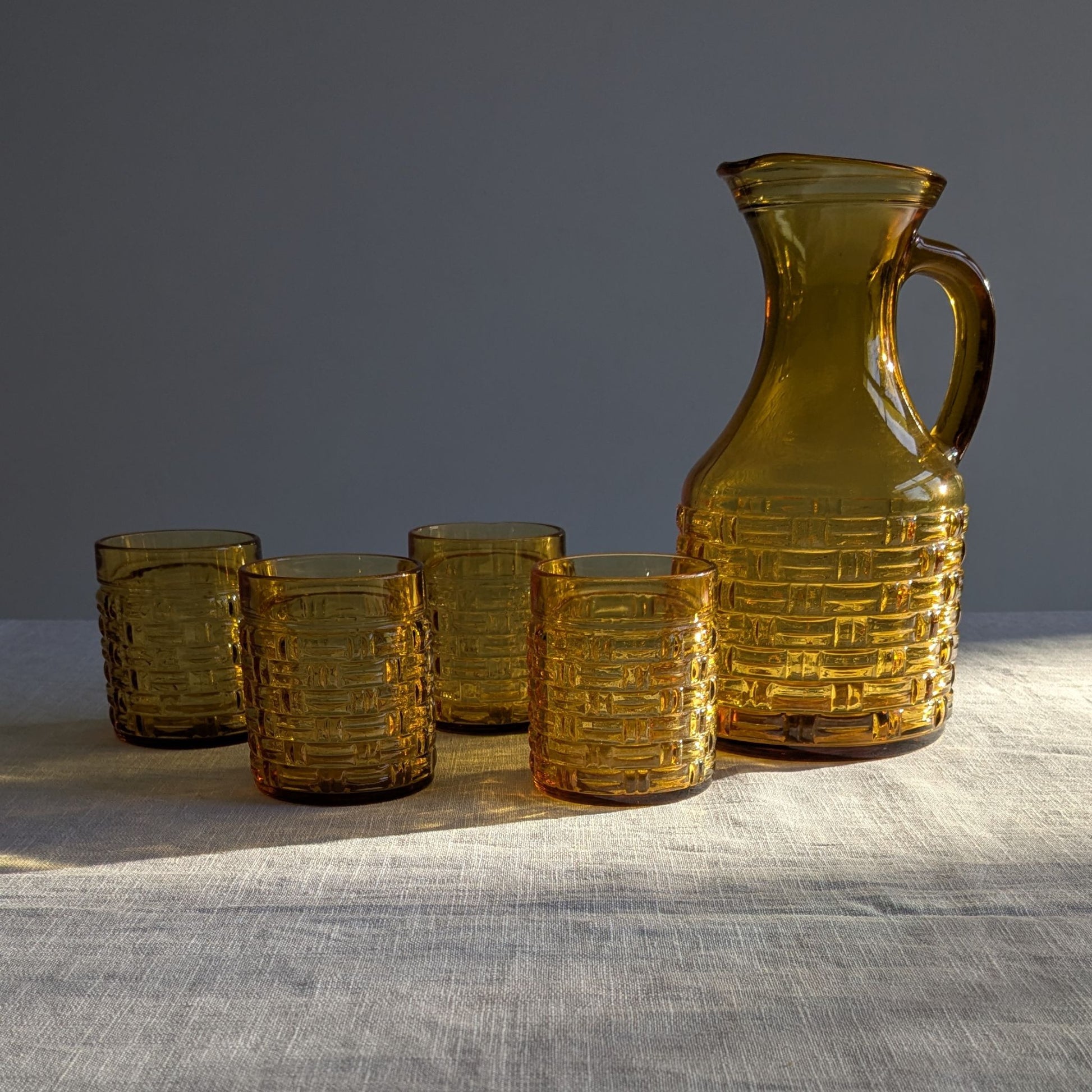 Yellow glass jug and four glasses in shadows