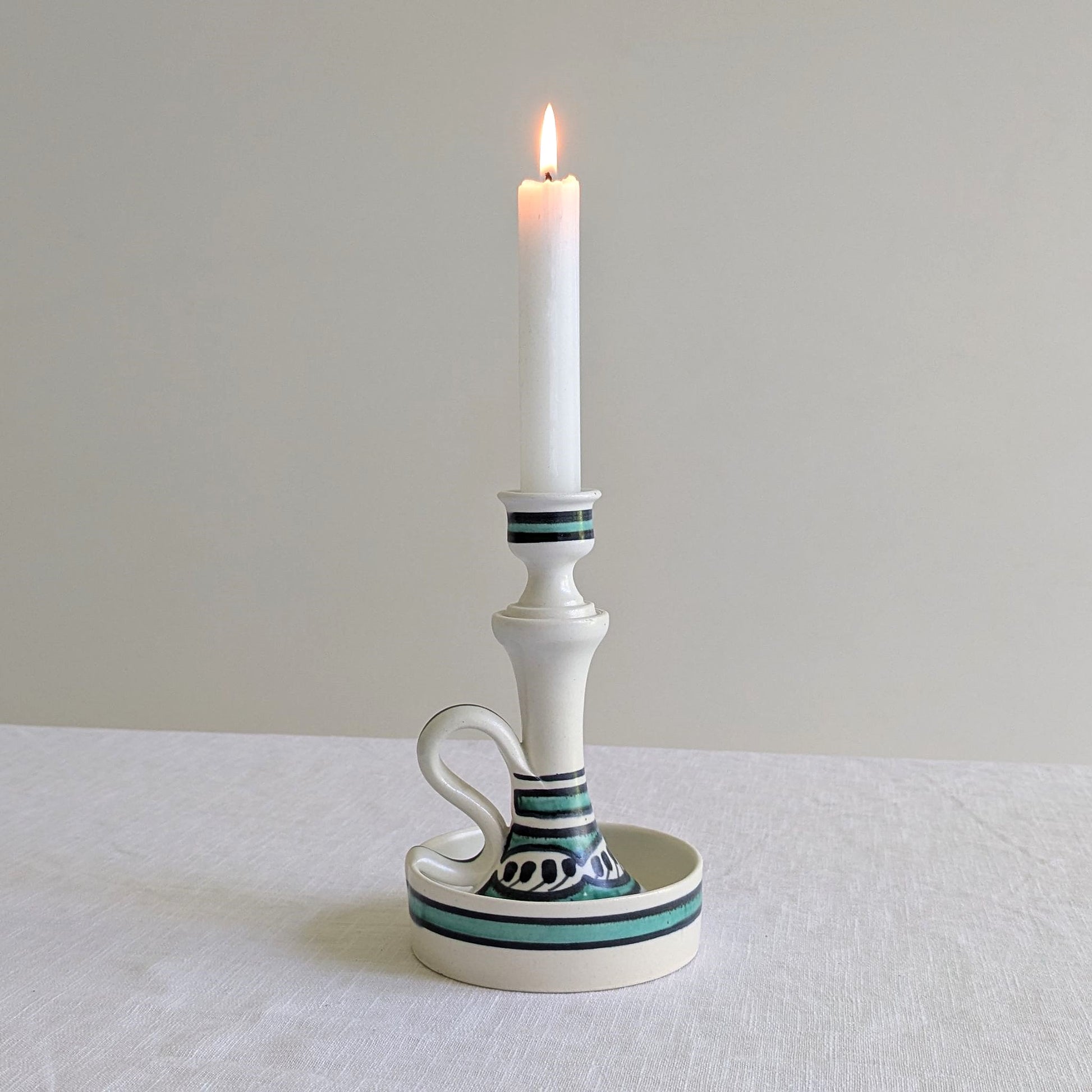 Tall white ceramic candle holder with a lit candle